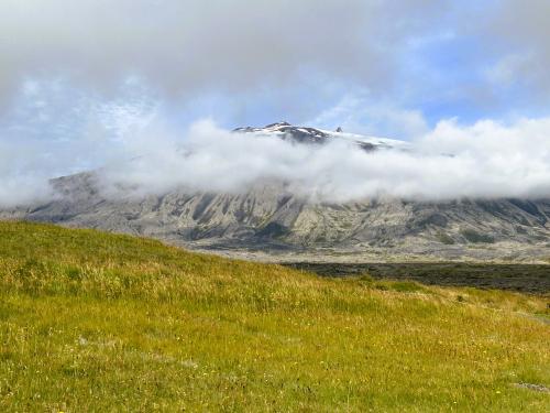 “In Sneffels Yoculis craterem kem delibat umbra Scartaris Julii intra calendas descende, audas viator, et terrestre centrum attinges. Kod feci” (Desciende al cráter del Yocul de Sneffels que la sombra del Scartaris acaricia antes de las calendas de Julio, audaz viajero, y llegarás al centro de la tierra, como he llegado yo). Esta es la traducción al latín (y al castellano) del texto de origen rúnico que ocultaba un criptograma del alquimista islandés Arne Saknussemm en el libro de Julio Verne “Viaje al centro de la Tierra”, publicado en 1864, en el que se revela cómo llegar al centro de la Tierra descendiendo por el volcán Snæfell.
Snæfellsjökull es un estratovolcán, cubierto por el glaciar del mismo nombre, situado en el extremo oeste de la península de Snæfellsnes, sobre la placa norteamericana. La zona de ruptura de Snæfellsnes se extendió activamente hasta hace unos 6 millones de años, cuando el límite de placas se desplazó hacia el este. Con unos 700.000 años de antigüedad, es uno de los cuatro sistemas volcánicos del cinturón volcánico de Snæfellsnes. La última erupción explosiva se produjo hace más de 1.100 años y arrojó 0,11 kilómetros cúbicos de material volcánico, formando el cráter actual que se eleva hasta los 1.446 metros sobre el nivel del mar. Posee numerosos conos piroclásticos laterales. Los conos de la parte superior de los flancos están formados por rocas de composición intermedia a félsica, mientras que los de la parte inferior son basálticos. (Autor: Antonio P. López)