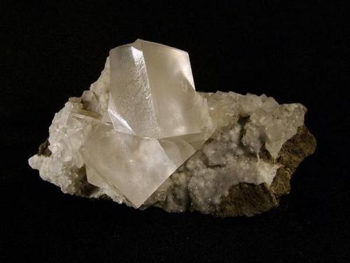 Calcite + stilbite
Biod a’ Mhurain, Duirinish, Isle of Skye, Scotland, UK
The large calcites 29 mm on edge

A beautiful specimen of transparent, slightly etched rhombohedral calcite with some modifications to the corners and edges. The large calcites (to 29mm on edge) rest on a bed of micro stilbite crystals and a few simple calcite rhombs. This is the first specimen I found at this locality; it was exposed to the atmosphere and colourless. The other calcites found within the cavity have a yellowish hue. Self-collected 1996 from Biod a’ Mhurain, Duirinish, Isle of Skye. (Author: Mike Wood)