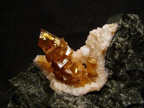 Calcite + chabazite + analcime
Talisker Bay, Isle of Skye, Scotland, UK
Calcite crystals 25 mm

Honey-brown spike of rhombohedral calcite crystals 25mm long stands in a vug (35mm x 20mm) lined with small twinned pinkish chabazite crystals and a single white analcime crystal (3mm). Self-collected 1992 from Talisker Bay, Isle of Skye. (Author: Mike Wood)