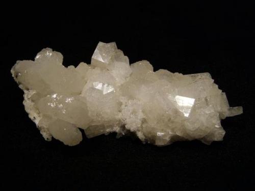 Chabazite + stilbite
Sgurr nam Boc, Isle of Skye, Scotland, UK
8 cm x 4 cm x 2 cm high

Fresh specimen measuring 8cm x 4cm x 2cm high. Simple clear and lustrous chabazite crystals to 14mm on edge, associated with lustrous flat-topped stilbites in curved aggregates, like cauliflower. Beneath is a thin crust made up of small stilbites, tiny quartz crystals and a little mordenite. Self-collected 1994 from Sgurr nam Boc, Isle of Skye. (Author: Mike Wood)