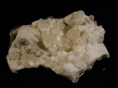 Calcite on basalt. Simple rhombs of transparent calcite to 11mm on edge rest on a bed of ’sugary’ looking calcite, which has a smooth surface. Specimen is 10cm x 8cm. Self-collected 1995 from Loch Bharcasaig, Duirinish, Isle of Skye. (Author: Mike Wood)