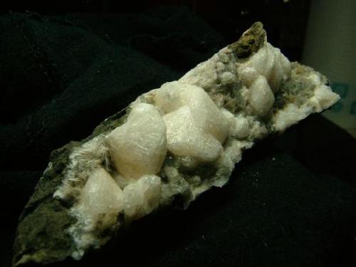 Chabazite variety ’phacolite’ + analcime + ’mesolite’
Oisgill Bay, Duirinish, Isle of Skye, Scotland, UK
Specimen is 12 cm long x 3 cm high x 5 cm deep
Chabazite crystals are up to 19 mm across

’Phacolite’ is an old name given to chabazites showing extreme twinning - these crystals are nearly circular! The crystals are up to 19mm across, and lie on a bed of very small grey (transparent) analcimes and some ’mesolite’ (could be natrolite as this mineral has been found here associated with analcime). Specimen is 12cm long x 3cm high x 5cm deep. Self-collected 1996 from Oisgill Bay, Isle of Skye. (Author: Mike Wood)