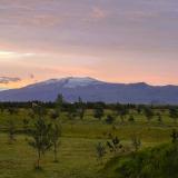 El volcán Eyjafjallajökull se encuentra entre el valle Þórsmörk, al norte, y la costa del océano Atlántico, al sur, en la región de Suðurland, al sur de Islandia. La capa de hielo del glaciar Eyjafjallajökull cubre el volcán, cuya parte superior está marcada por una profunda depresión que corresponde a la caldera, de 2,5 km de diámetro. El pico más alto es una parte del borde del cráter, llamado Hámundur, con 1.651 m de altura sobre el nivel del mar. Es un estratovolcán formado por basalto y andesita, hace unos 700.000 años, que una vez fue parte de la costa del océano Atlántico. La llanura que se extiende desde su pie hasta la costa del océano se formó por el depósito sucesivo de materiales, incluyendo hialoclastitas, arrastrados por las inundaciones causadas por diversas erupciones subglaciales.
En la imagen, el volcán y glaciar Eyjafjallajökull al amanecer visto desde las praderas del distrito Eyjafjallaveist. (Autor: Antonio P. López)