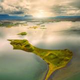 El lago Mývatn, en el municipio de Skútustaðahreppur, al norte de Islandia, con 37 km2 de superficie y 4,5 metros de profundidad máxima, alberga una serie de curiosos cráteres que afloran en su superficie, son los Skútustaðagígar. La traducción al castellano es literalmente "cráteres de Skútustaðir", y son un conjunto de ‘pseudocráteres’ situados en la costa sur del lago. El apelativo de ‘pseudocráteres’ se lo dio el geólogo y vulcanólogo islandés Sigurður Þórarinsson porque nunca llegaron a emitir lava. Según su teoría, Skútustaðir se creó hace aproximadamente 2.300 años, durante la erupción simultánea del Lúdentaborgir y el Þrengslaborgir, del sistema volcánico Krafla. En su avance, la lava alcanzó una zona pantanosa o un lago somero muy parecido al actual Mývatn. El enorme calor evaporó casi inmediatamente el agua superficial, pero aquella que se encontraba a mayor profundidad se fue calentando más lentamente. Mientras tanto, el peso de la lava acumulada en la superficie aumentaba la presión sobre la mezcla de sedimentos y agua. Finalmente, el agua acabó abriéndose camino en forma de vapor a través de la colada en una serie de erupciones explosivas que formaron estos conos.
Foto tomada con dron por Carlos Martín Ayala (Autor: Antonio P. López)